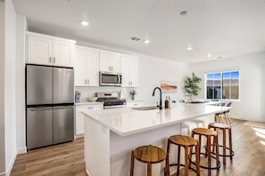 A modern kitchen with white cabinetry, stainless steel appliances, and a large island with bar stools. - Brand New Skyline Resort 1737, Private Hot tub, Resort Access, & Near Sand Hollow Lake (Washington)