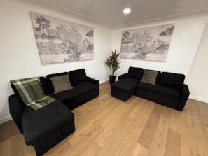 Ein Wohnzimmer mit zwei schwarzen Sofas, einer grünen karierten Decke und einer Topfpflanze.