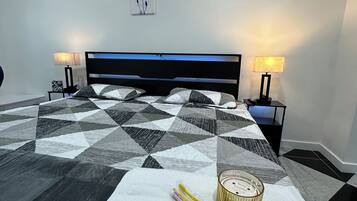 Een net opgemaakt bed met een sprei met een geometrisch patroon, twee bedlampen en wanddecoratie.
