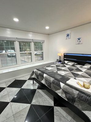 Ein Schlafzimmer mit Bett, einem Fenster mit Blick auf parkende Autos und einem gefliesten Boden.