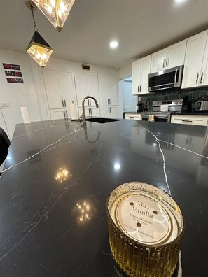 Una cocina moderna con gabinetes blancos, encimera de mármol negro, electrodomésticos de acero inoxidable y una vela decorativa.