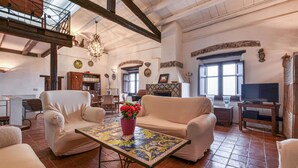 Un salón espacioso con techo alto, una araña, chimenea y televisor.