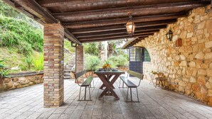 Un patio techado con muro de piedra, una mesa de madera con sillas y un farol.