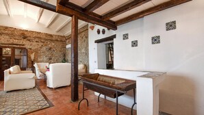 Interior rústico con paredes de piedra, un banco de madera, muebles blancos y suelo de baldosas.