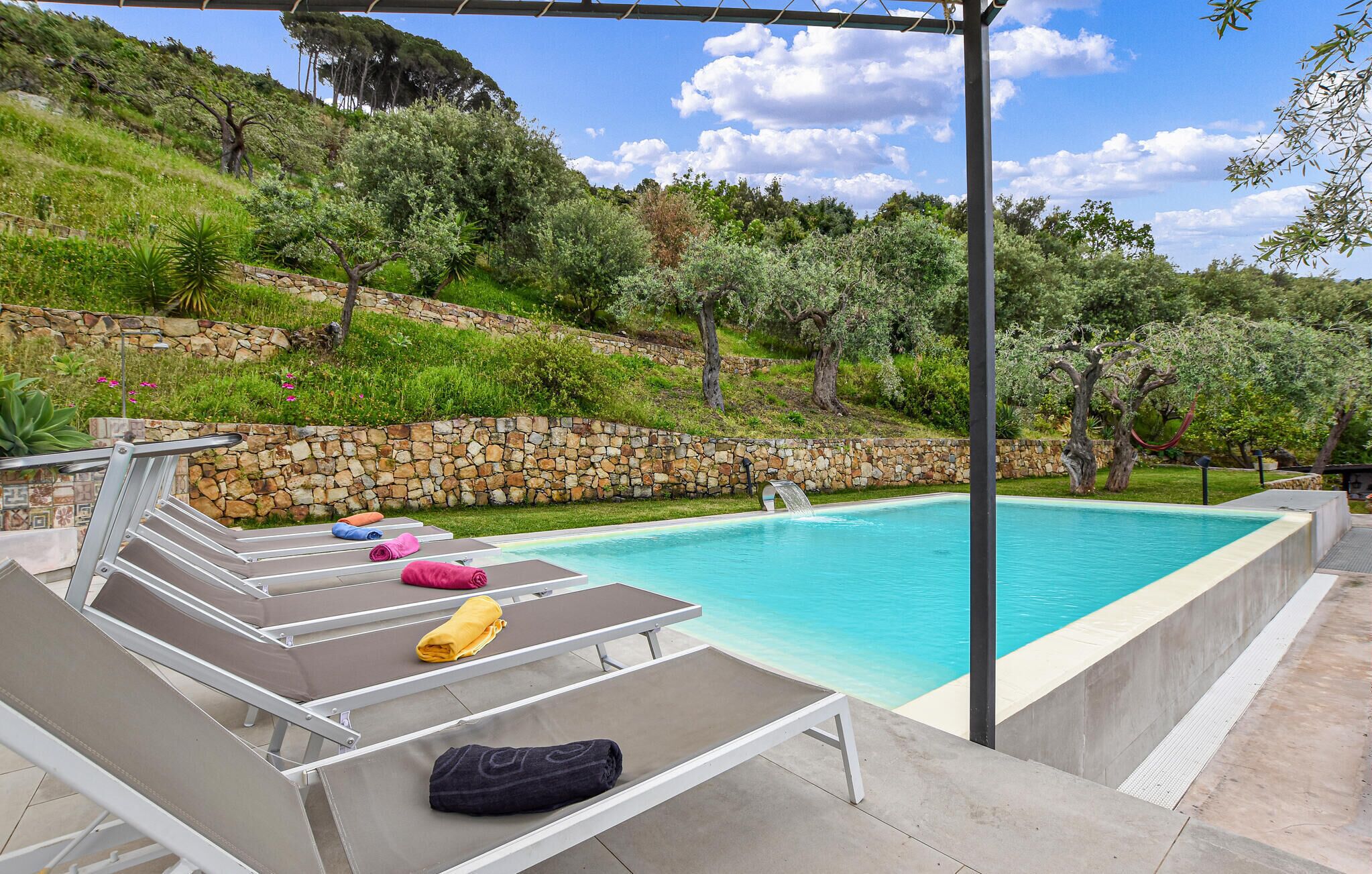 A swimming pool with lounge chairs and a stone wall.