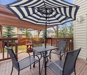 A patio with a table and chairs, a fire pit, and a large striped umbrella. - King Bed, 75 min Banff, Backyard and Wood Fire BBQ (Calgary)