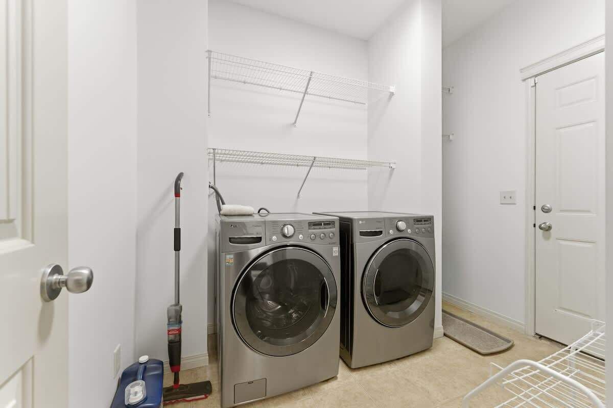 A laundry room with two front-loading washing machines, a drying rack, and a broom.