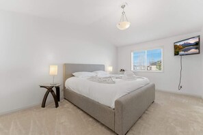 A bedroom with a bed, bedside lamps, a window with blinds, a TV mounted on the wall, and a ceiling light. - King Bed, 75 min Banff, Backyard and Wood Fire BBQ (Calgary)