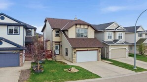 A residential house with a garage, a driveway, and a small lawn with a tree. - King Bed, 75 min Banff, Backyard and Wood Fire BBQ (Calgary)