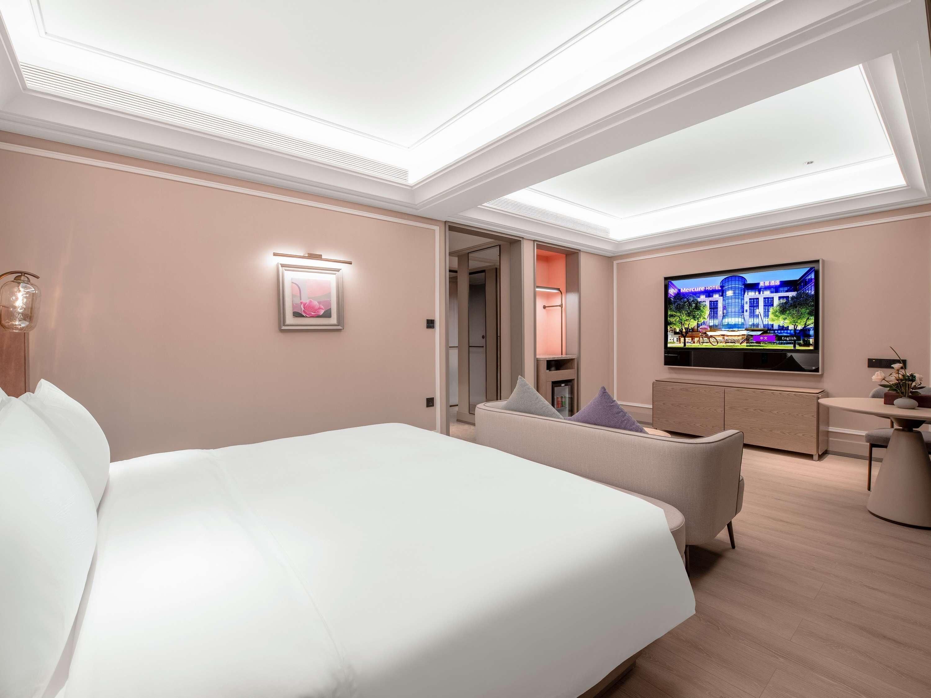 Une chambre d’hôtel avec un grand lit, une télévision, un coin salon et une porte donnant sur une salle de bain.