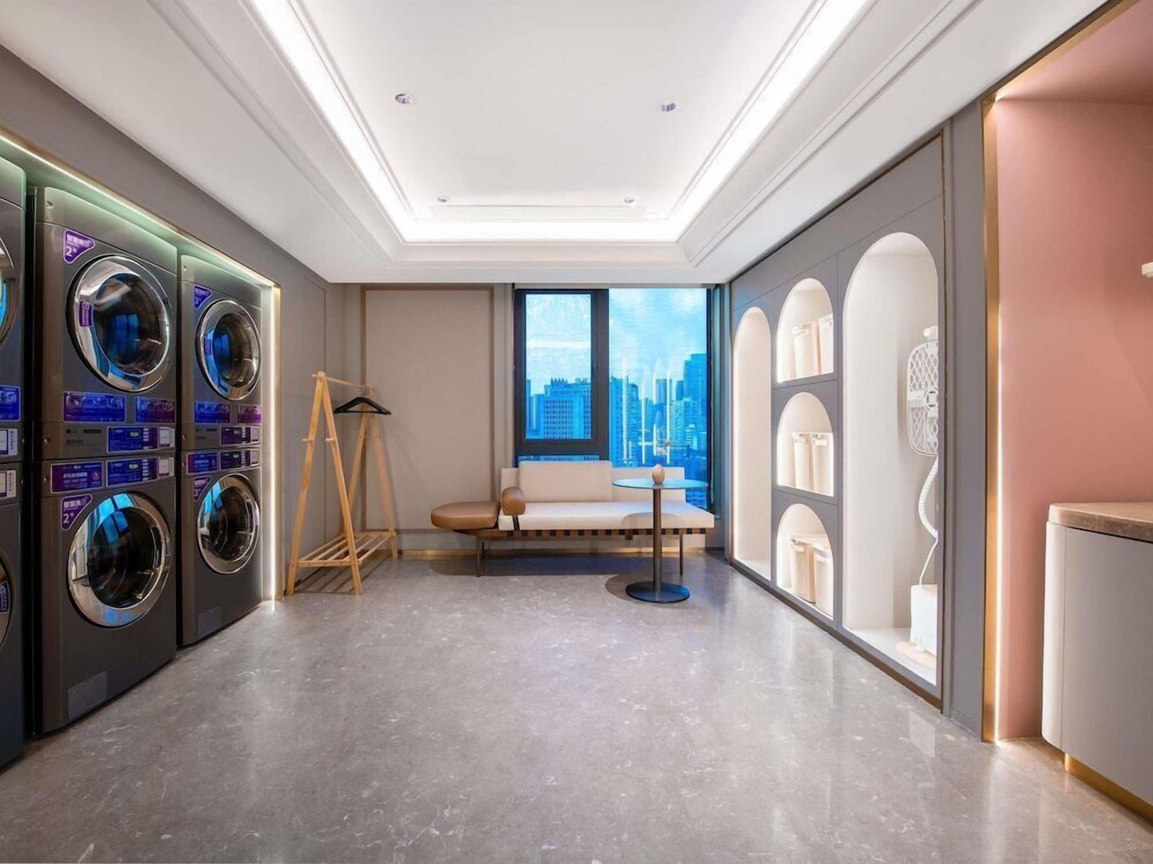 A hotel room with a city view, a sofa, a small table, and a washing machine.