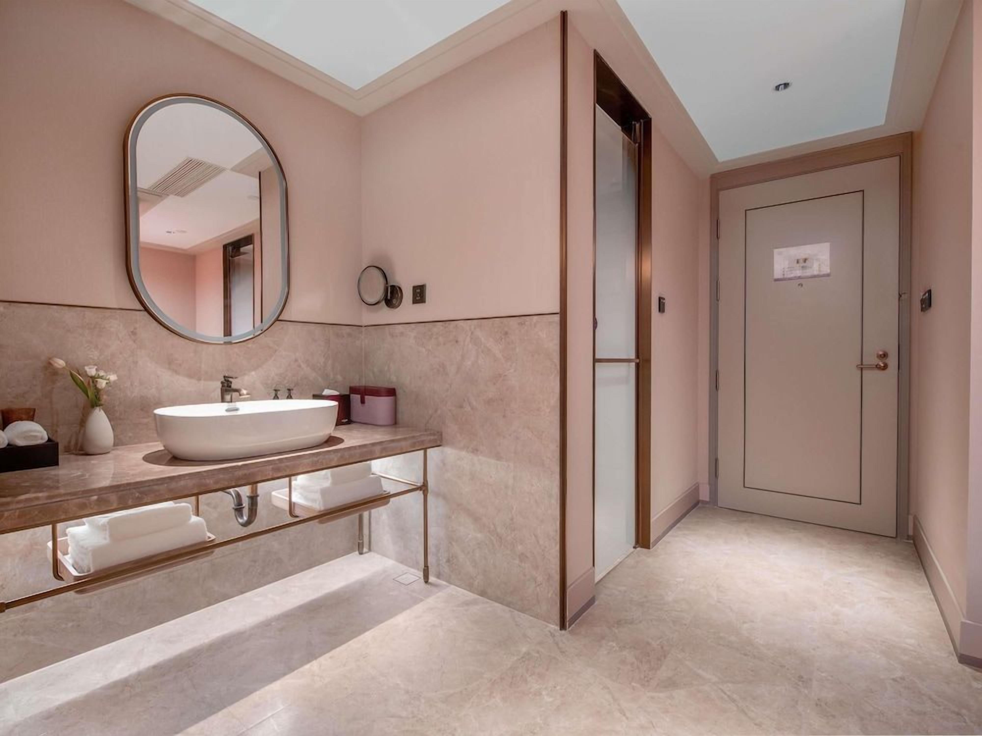 A modern bathroom with a large oval sink, a mirror, and a door leading to another room.