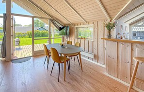 A wooden interior with a dining table, chairs, a TV, and a view of a green garden. - Cozy home in Dannemare with WiFi (Dannemare)