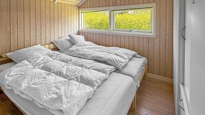 A room with wooden walls, a window with a view of greenery, and a bed with white bedding. - Cozy home in Dannemare with WiFi (Dannemare)