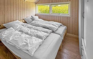 Ein Zimmer mit Holzwänden, einem Fenster mit Blick ins Grüne und einem Bett mit weißer Bettwäsche.