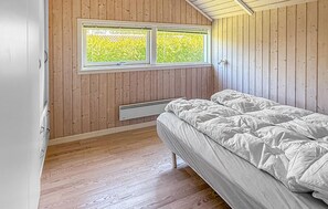 A room with wooden walls, a window with a view of greenery, a bed with white bedding, and a radiator under the window. - Cozy home in Dannemare with WiFi (Dannemare)
