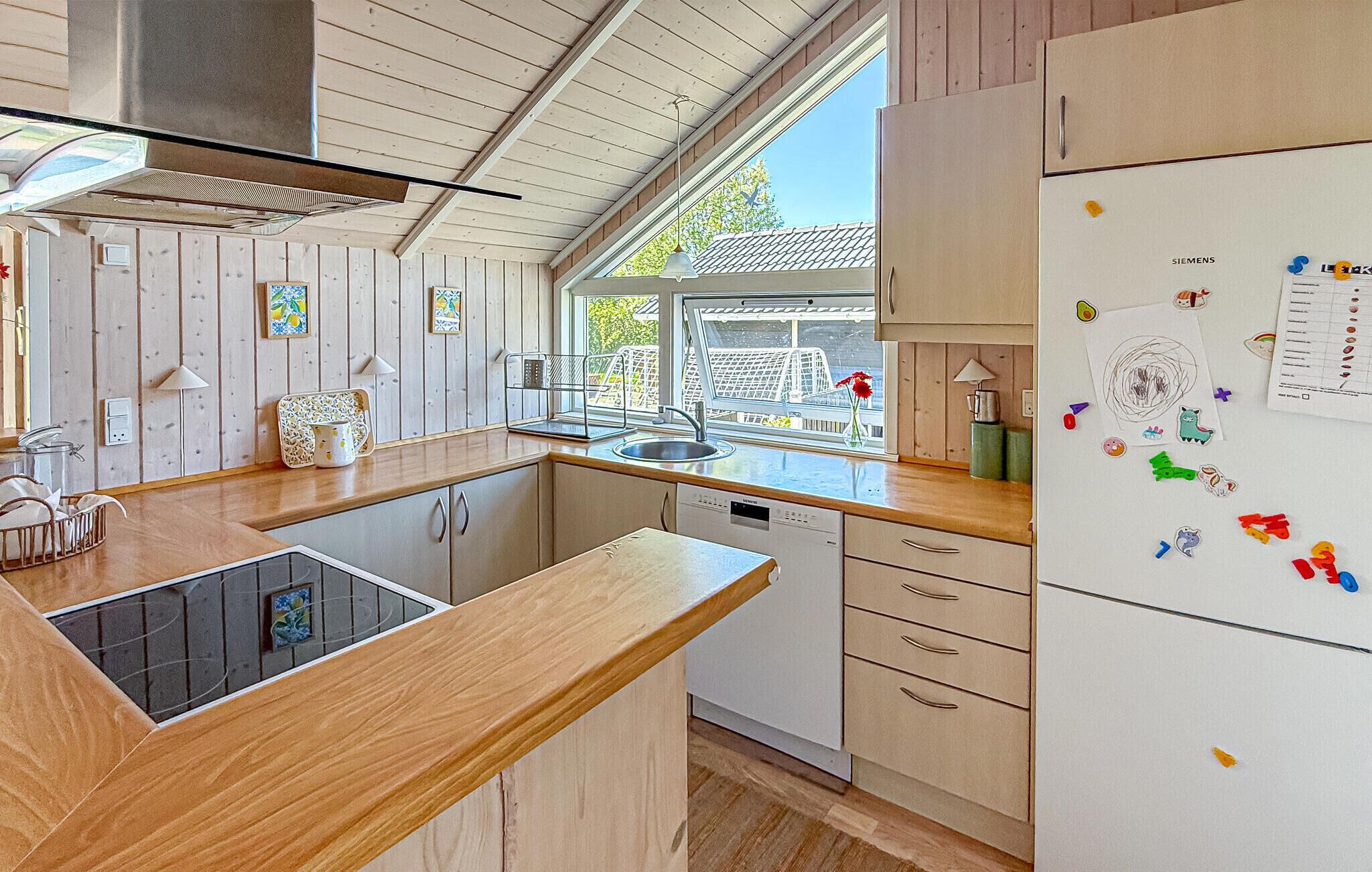 A modern kitchen with wooden cabinets, a built-in dishwasher, a stainless steel sink, and a refrigerator with magnets.