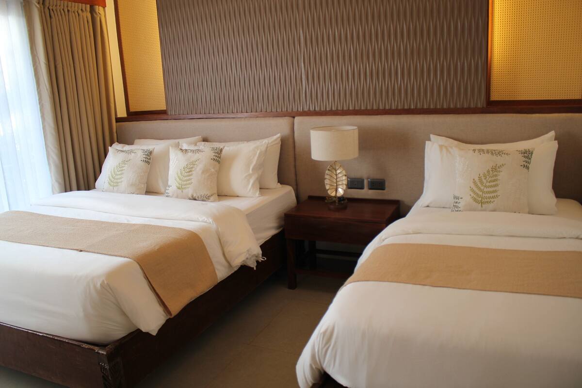Habitación de hotel con dos camas, una mesita de noche con lámpara y pared con textura.