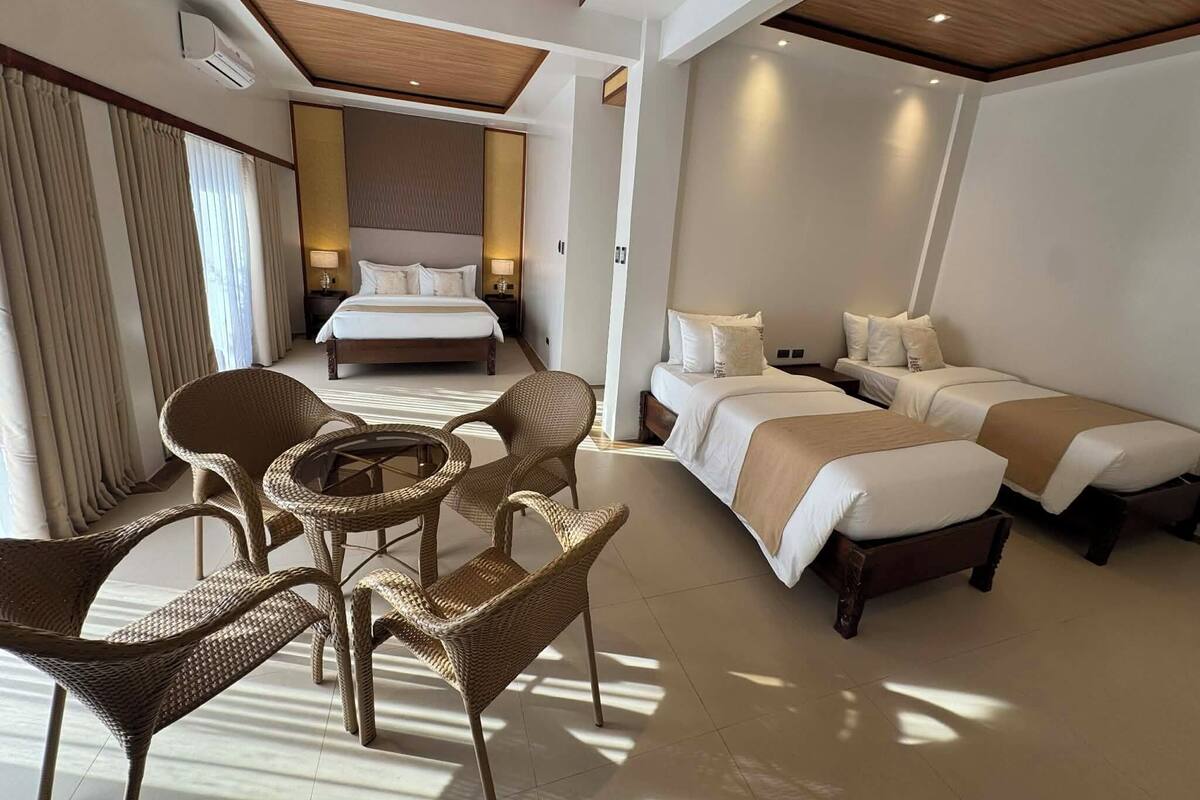 Una habitación de hotel con una cama grande, dos camas más pequeñas, muebles de mimbre y un techo con vigas de madera.