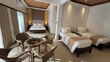 A hotel room with a large bed, two smaller beds, wicker furniture, and a ceiling with wooden beams.