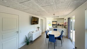 Una cuina moderna amb armaris blancs, una zona de menjador amb taula rodona i cadires blaves, i un sostre amb un disseny texturat.