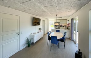 Eine moderne Küche mit weißen Schränken, einem Essbereich mit rundem Tisch und blauen Stühlen sowie einer Decke mit Strukturmuster.
