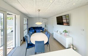 Ein moderner Essbereich mit einem runden Tisch, blauen Stühlen, einer weißen Konsole und einem an der Wand befestigten Fernseher.