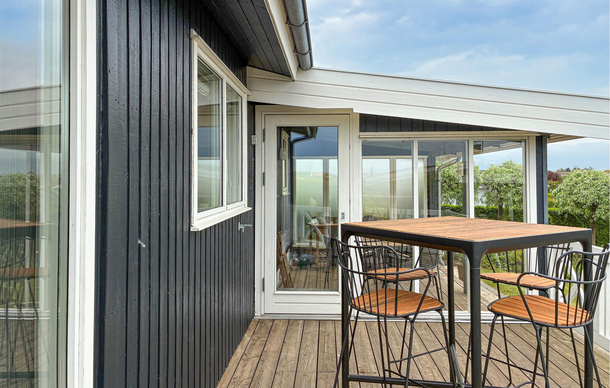 A modern house with a wooden deck, a glass door leading to a patio, and a table with chairs.