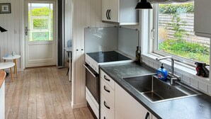 Une cuisine moderne équipée d’une cuisinière intégrée, d’un évier et d’une fenêtre donnant sur un espace verdoyant.
