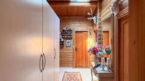 Un couloir intérieur aux murs en bois, avec une porte en bois, un miroir, un vase de fleurs et un tapis à motifs.