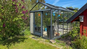 Une serre dotée d’un toit en verre, entourée de verdure et bordée d’un bâtiment rouge.