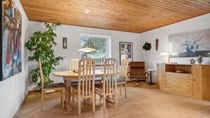 Et spiseområde med et træbord og stole, en potteplante og et vindue med udsigt til træer.