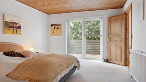 Et soveværelse med seng, træloft, skydedør til en balkon og et træskab.