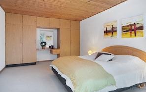 A bedroom with a bed, wooden wardrobe, bedside table, lamp, and two wall-mounted paintings.