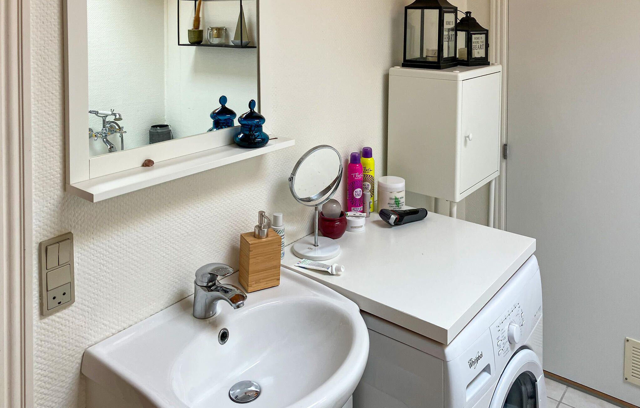 Ein Badezimmer mit Waschbecken, Spiegel, Zahnbürstenhalter und einer Waschmaschine.