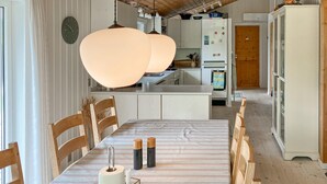 A dining area with a striped tablecloth, wooden chairs, a hanging light fixture, and a kitchen in the background. - Awesome home in Farsø with sauna (Farsø)