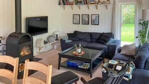 A cozy living room with a fireplace, a sofa, a coffee table, and a television. - Awesome home in Farsø with sauna (Farsø)