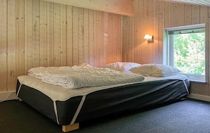 A single bed with a black frame and white bedding in a room with wooden walls and a window with a view of greenery. - 4 bedroom gorgeous home in Farsø (Farsø)