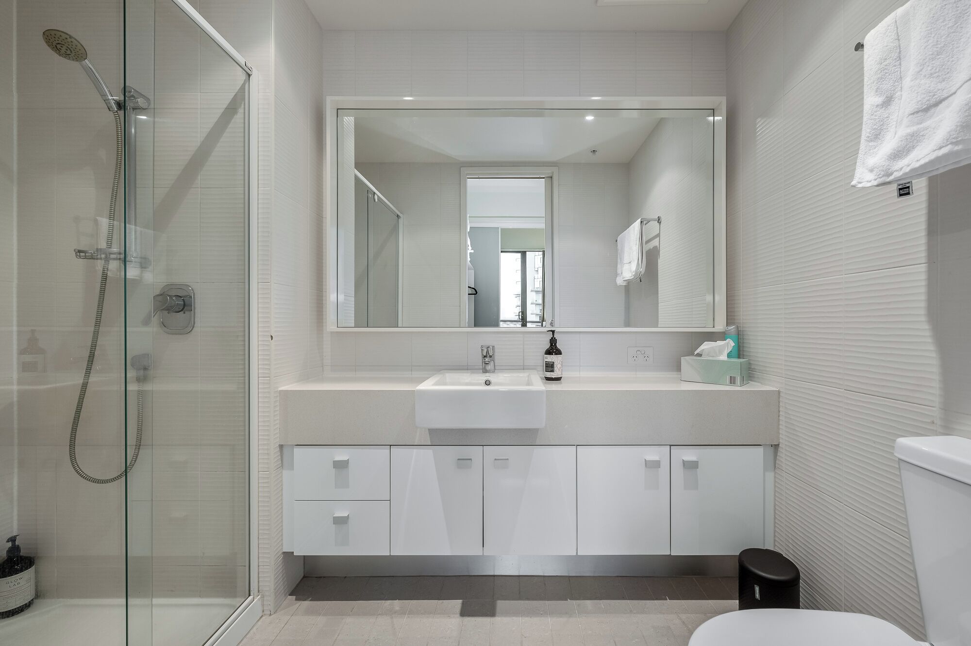 A modern bathroom with a glass shower enclosure, a white sink, and a large mirror above the vanity.