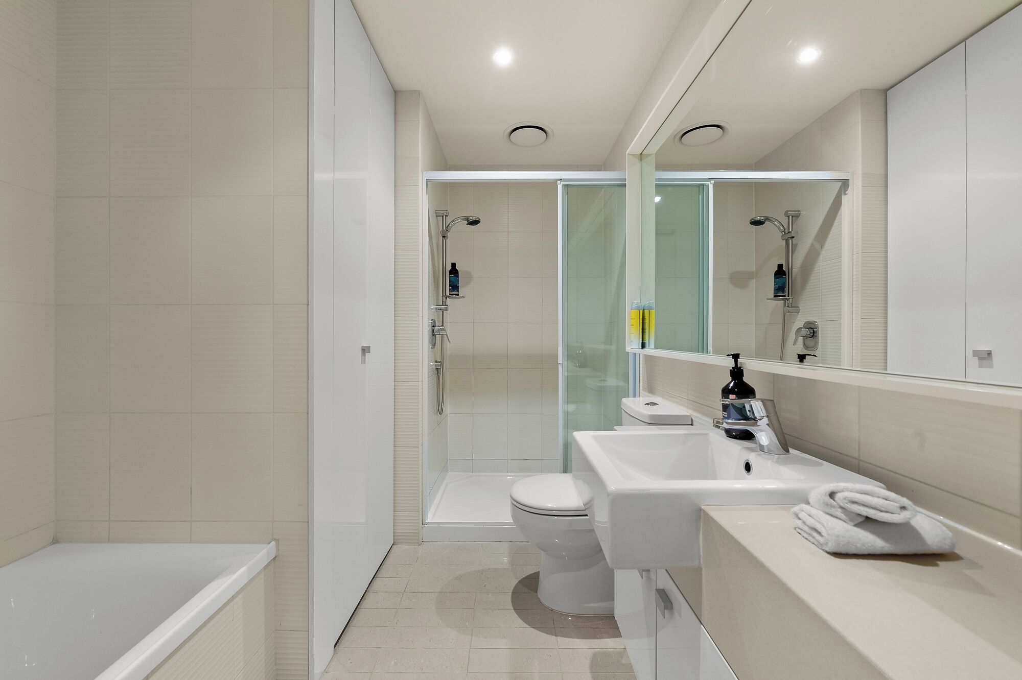A modern bathroom with a glass-enclosed shower, a white toilet, and a sink with a mirror above it.
