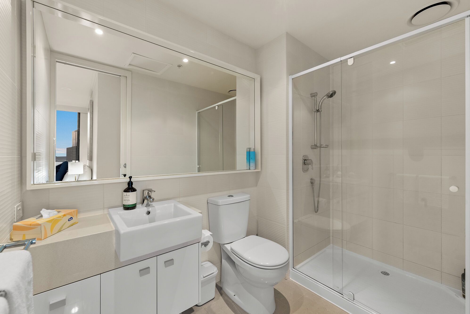 A modern bathroom with a large mirror, a sink, a toilet, and a glass-enclosed shower.
