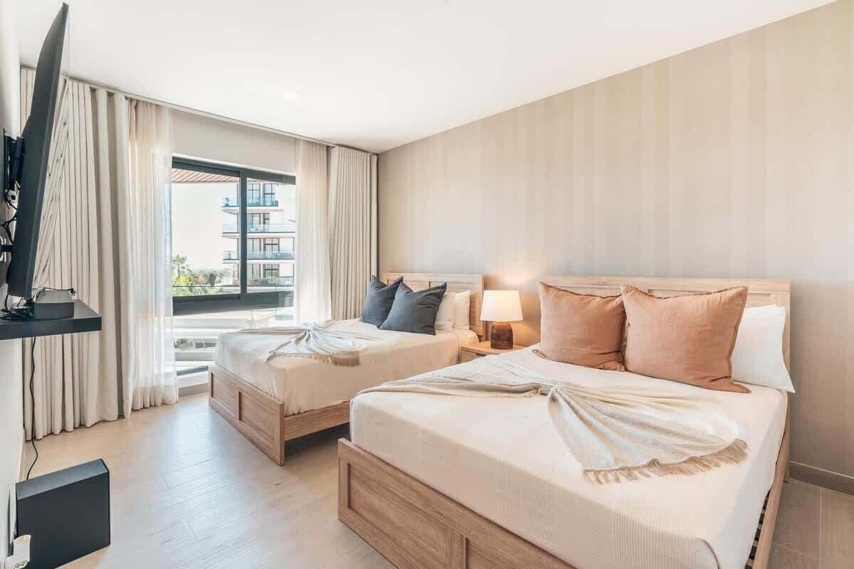 Ein Hotelzimmer mit zwei Betten, einem Fernseher und einem Balkon mit Vorhängen.