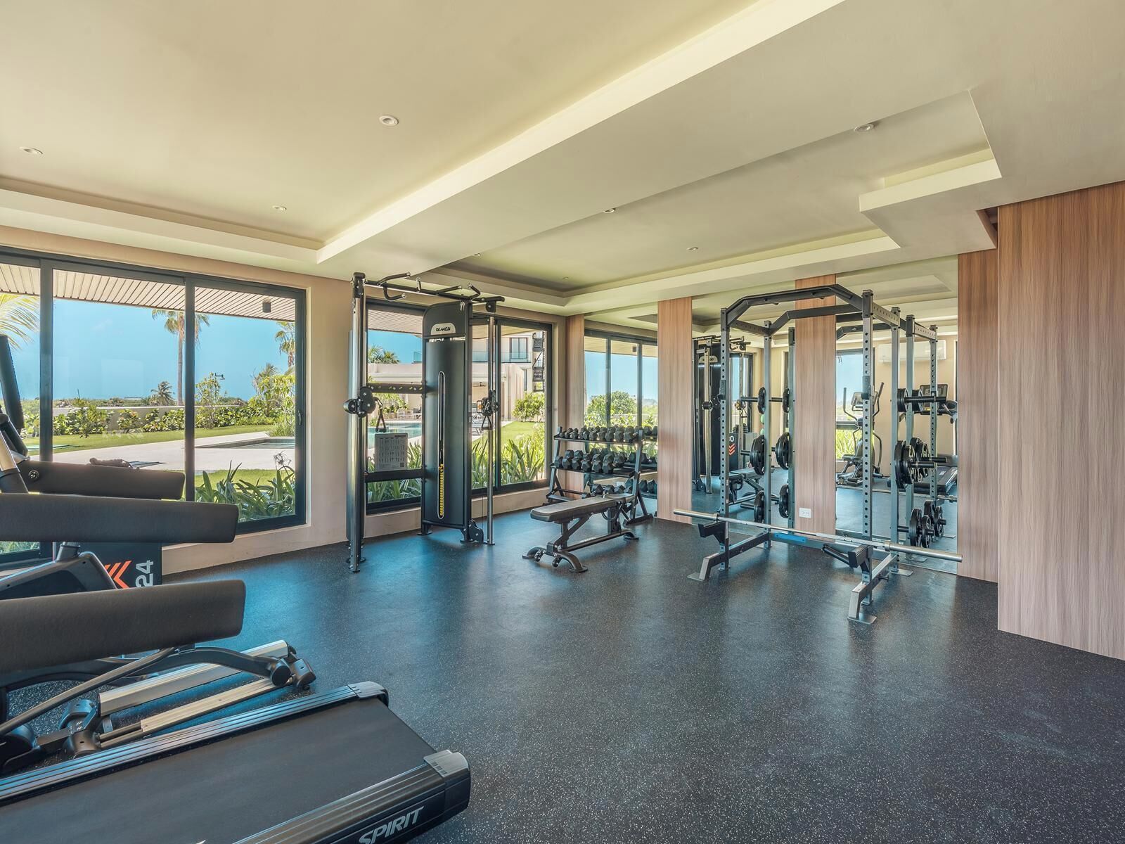 Un gimnasio espacioso con diversos equipos de ejercicio, amplias ventanas que ofrecen vistas al exterior y un diseño interior moderno.