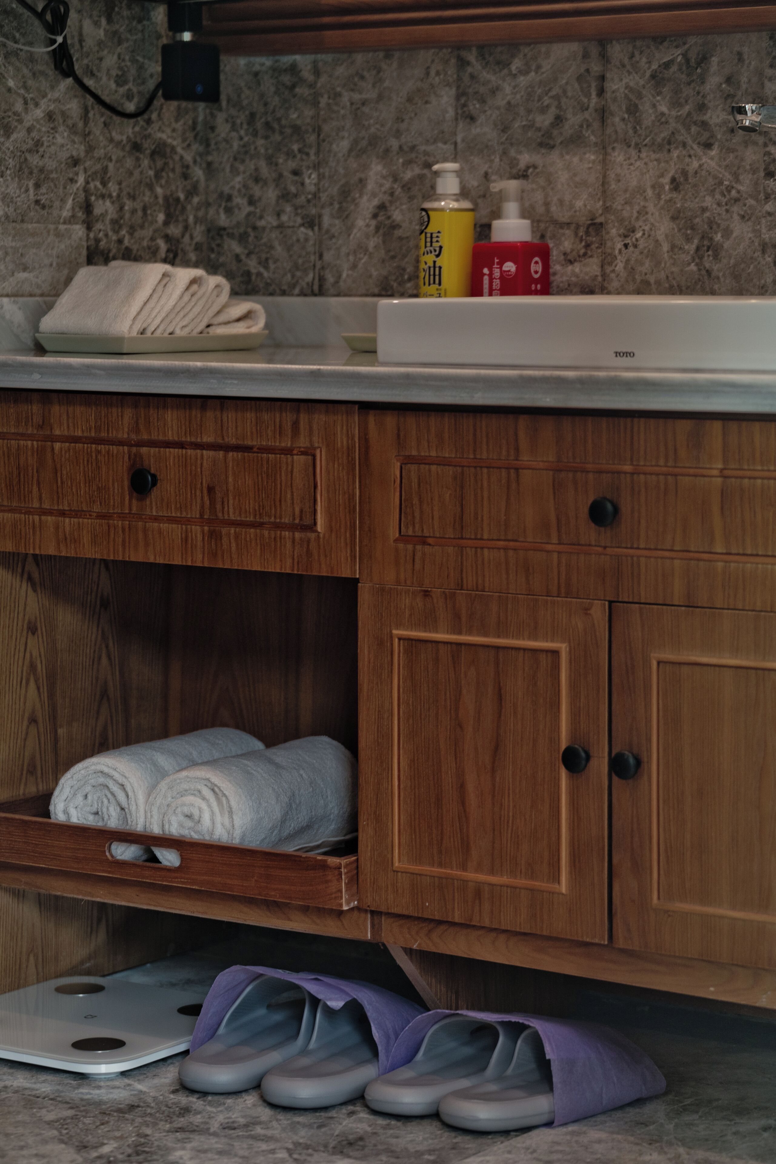 A bathroom with a marble wall, wooden cabinets, a towel rack, and a scale.