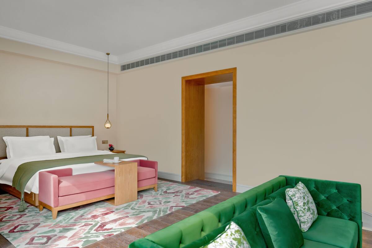 Une chambre à coucher avec un lit, un canapé vert, un canapé rose, une table de chevet et un tapis à motifs.