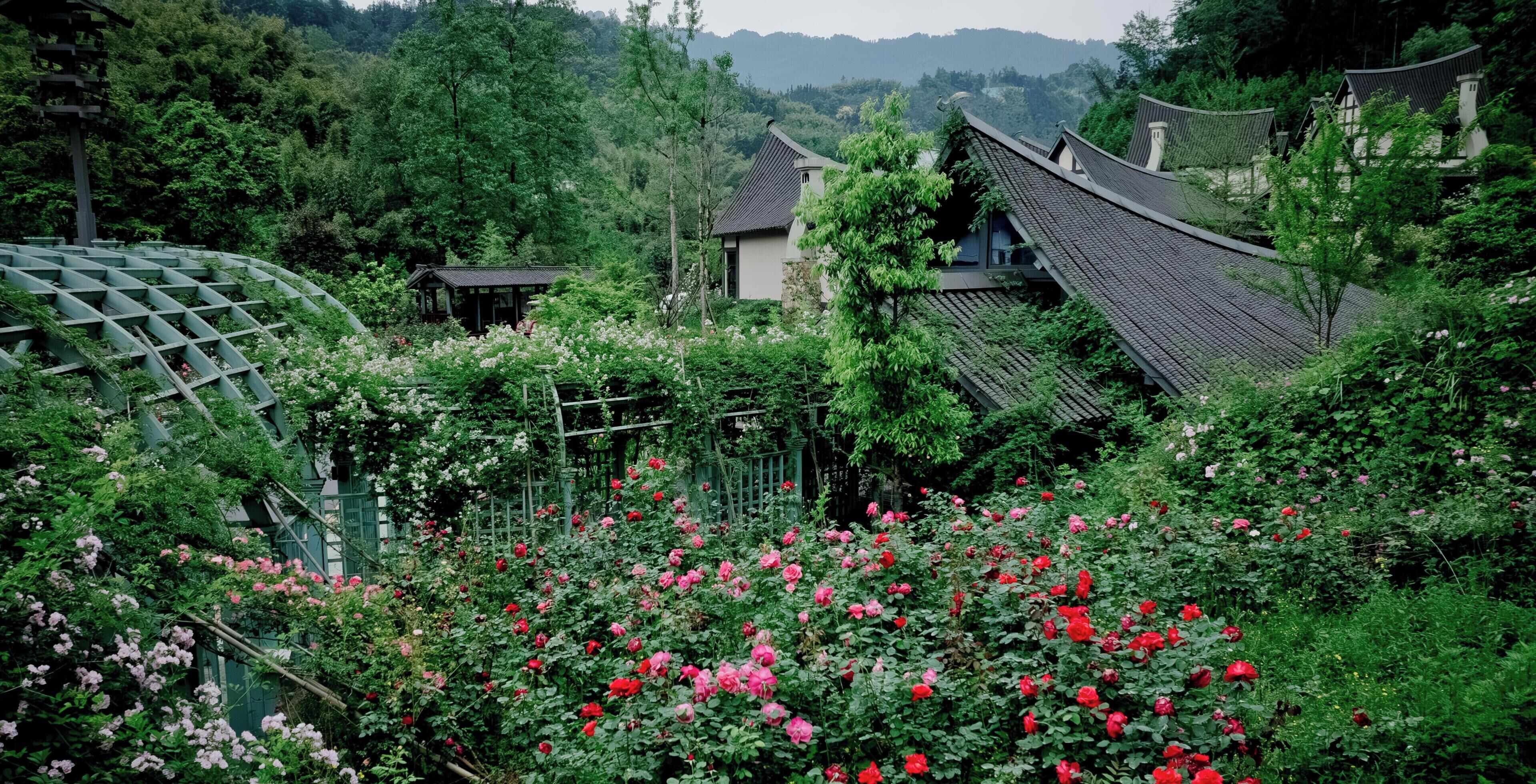 Un jardín japonés tradicional con un pabellón de madera, una construcción pequeña y una casa con tejado de tejas.