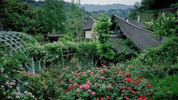 Un jardín japonés tradicional con un pabellón de madera, una construcción pequeña y una casa con tejado de tejas.