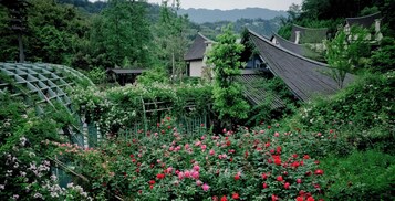 Un jardín japonés tradicional con un pabellón de madera, una construcción pequeña y una casa con tejado de tejas.