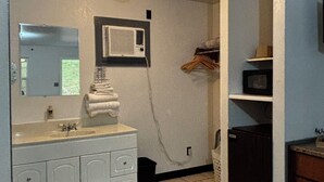 Un baño con lavamanos, espejo, toallero y un equipo de aire acondicionado en la pared.