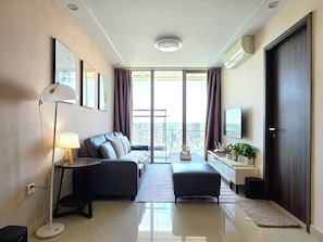 Quarto de hotel moderno com sofá, escrivaninha, luminária, televisão e uma janela grande com vista para a cidade.
